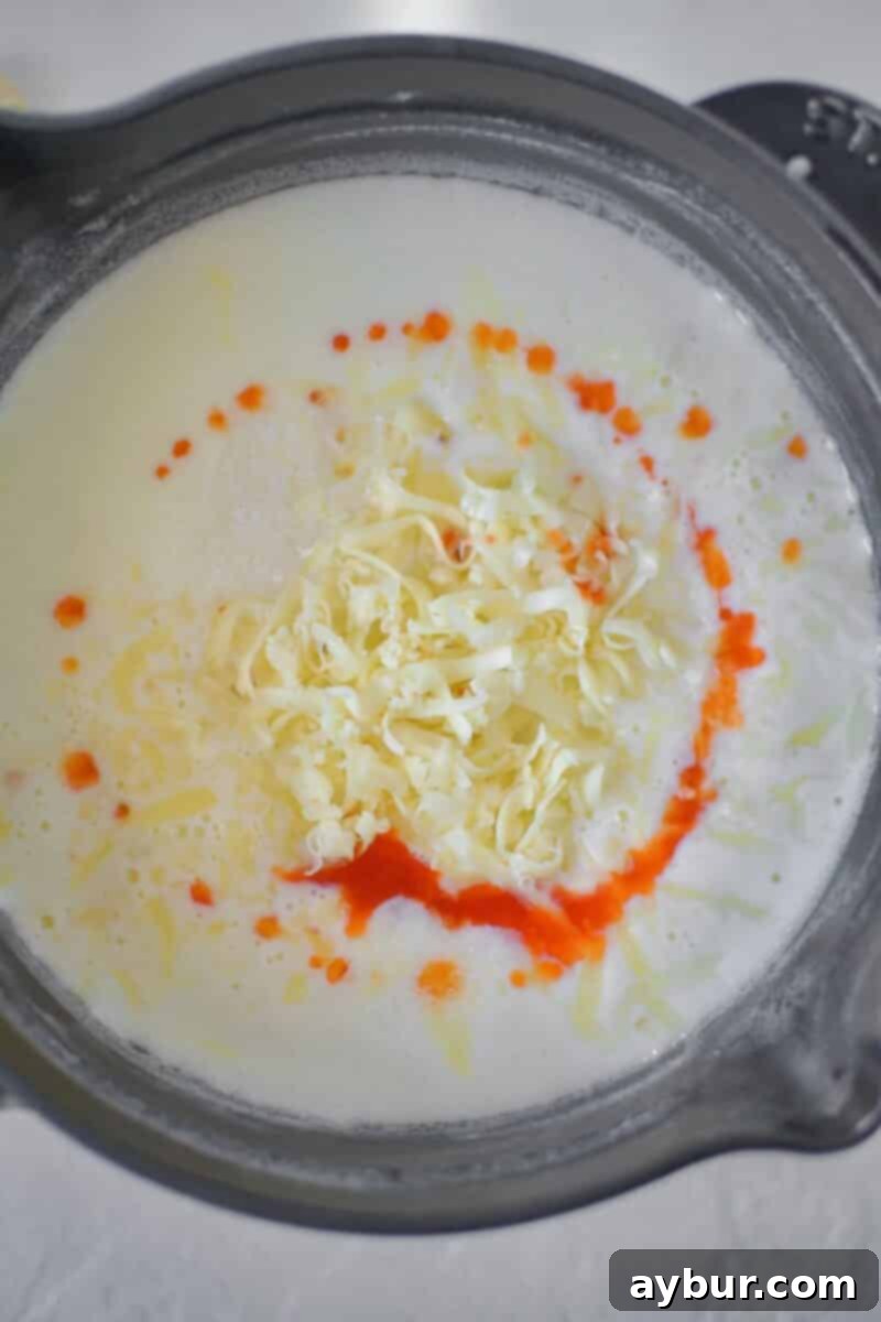 Creamy White Queso 6 A close-up view of melted cheese and hot sauce swirling together in a saucepan, creating a vibrant base for the queso dip.