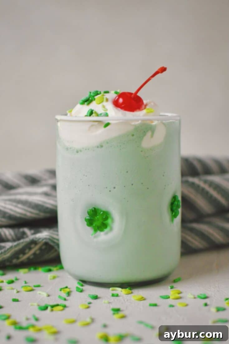 A vibrant green Shamrock Shake in a festive shamrock-patterned glass, generously topped with fluffy whipped cream, colorful sprinkles, and a bright red cherry, perfect for St. Patrick's Day celebrations.