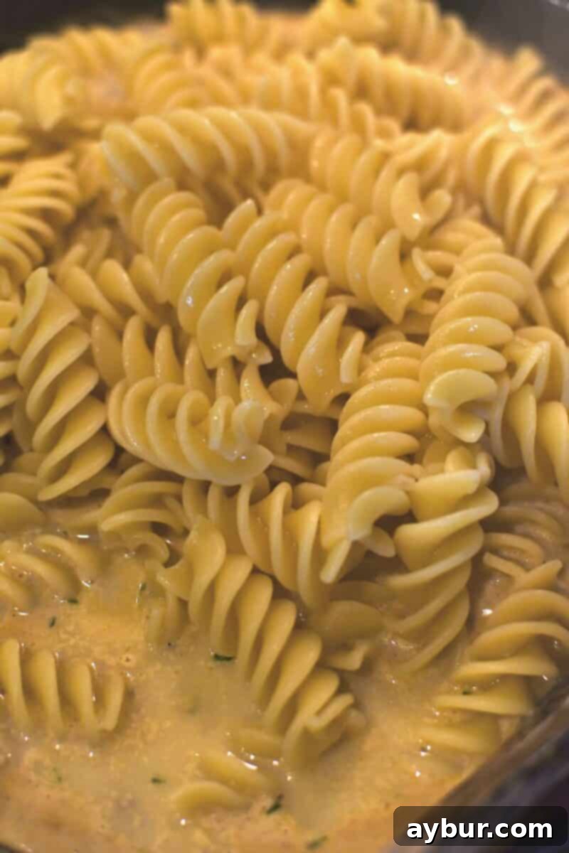 Cooked pasta being added to the rich, creamy Cajun Alfredo sauce in a large skillet, ready to be tossed and combined.