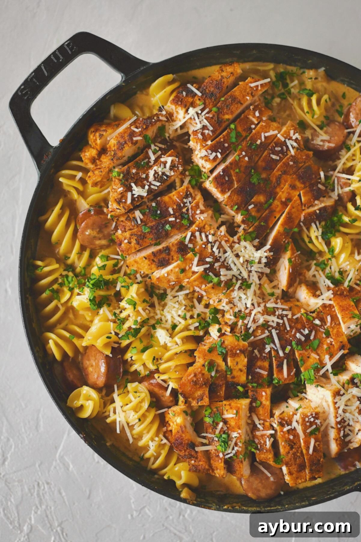 A large skillet filled with creamy Cajun Chicken Alfredo, topped with sliced blackened chicken and a sprinkle of fresh green parsley, ready to serve.