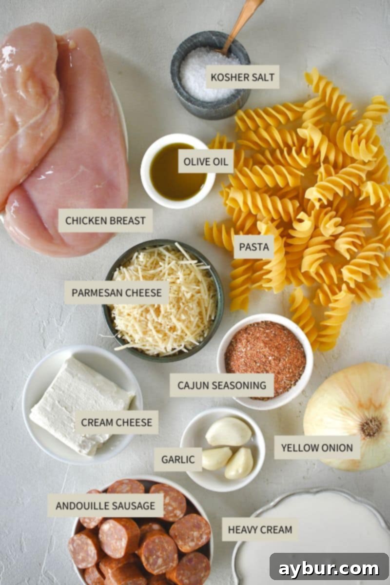 A vibrant selection of ingredients for Cajun Chicken Alfredo, including raw chicken breasts, fresh parsley, onion, garlic, pasta, cream, cream cheese, and a container of Cajun seasoning.