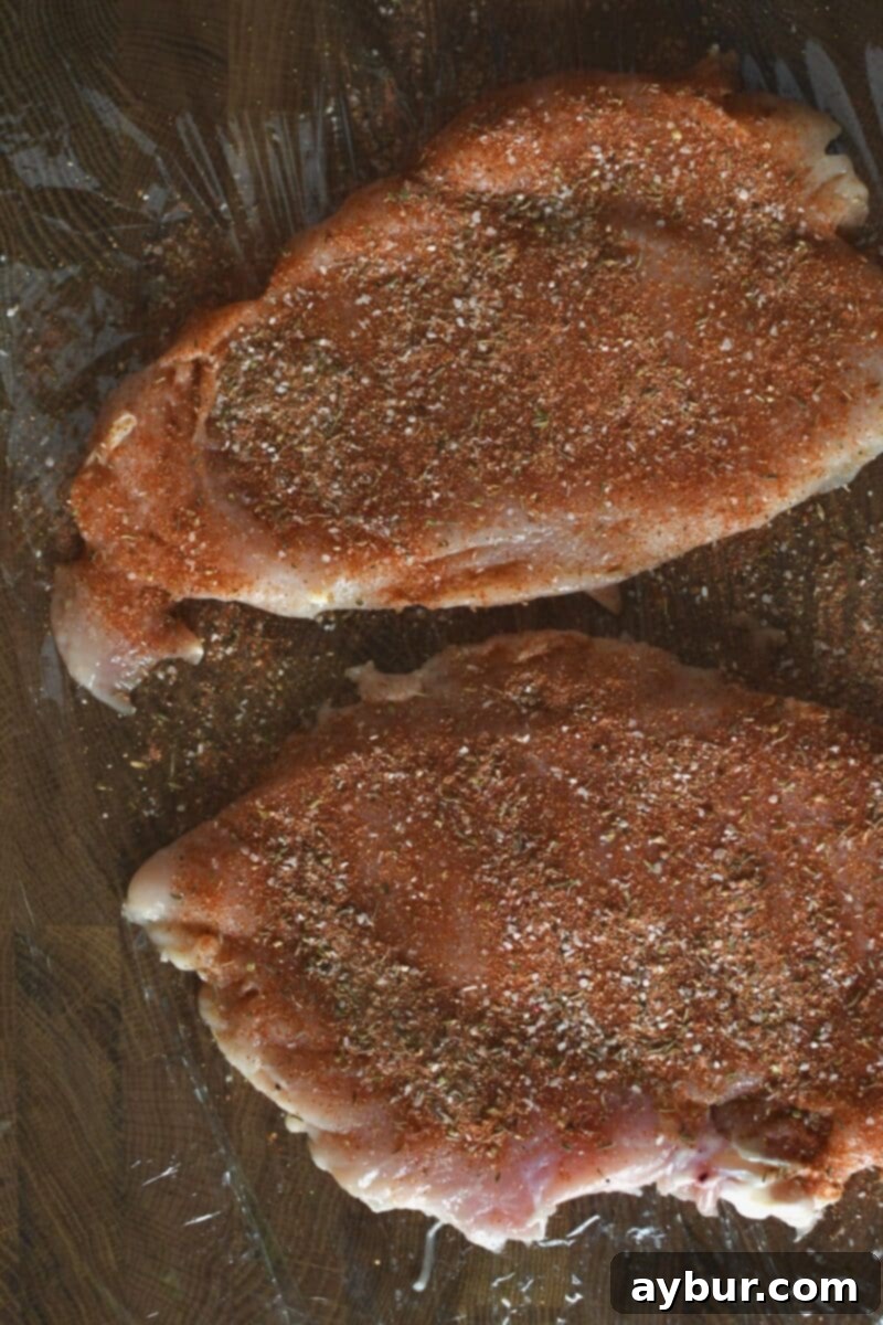 Flattened chicken breasts generously seasoned with dark red Cajun seasoning on a cutting board.