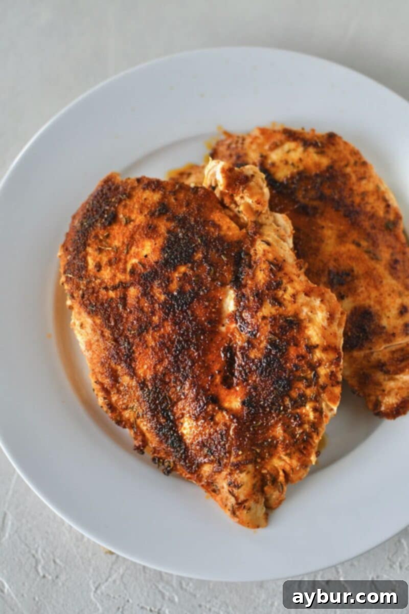 Two pieces of chicken breast with a dark, rich blackened crust after searing in a hot pan.