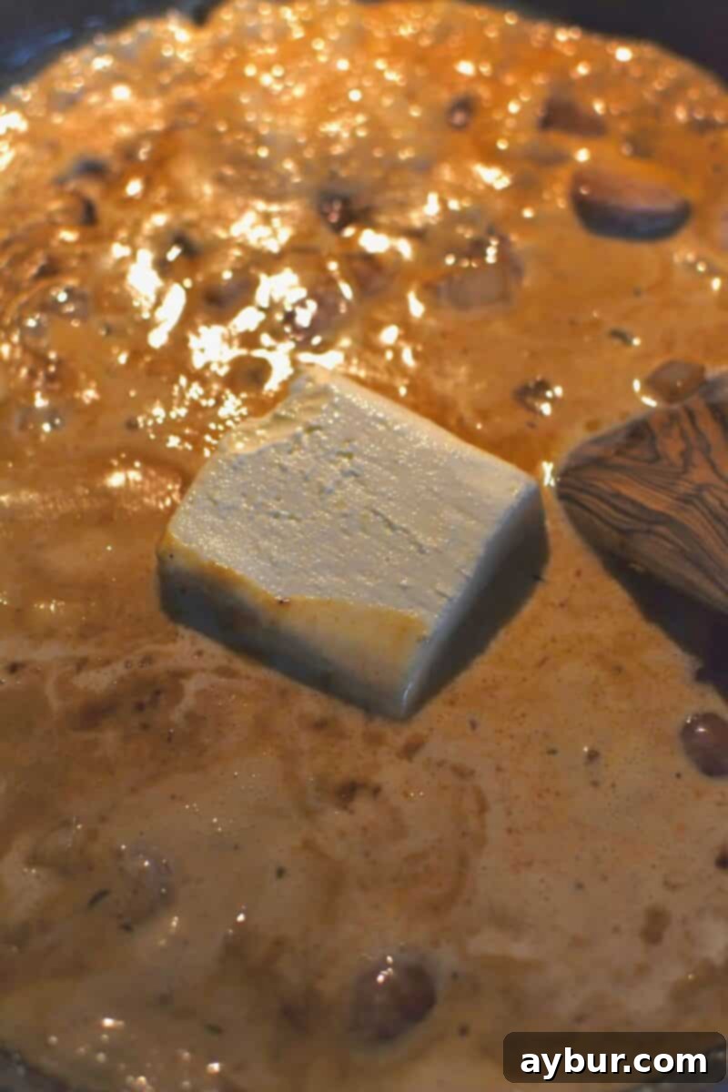 Heavy cream and softened cream cheese added to the skillet with cooked onions, garlic, and sausage, ready to form the Alfredo sauce.