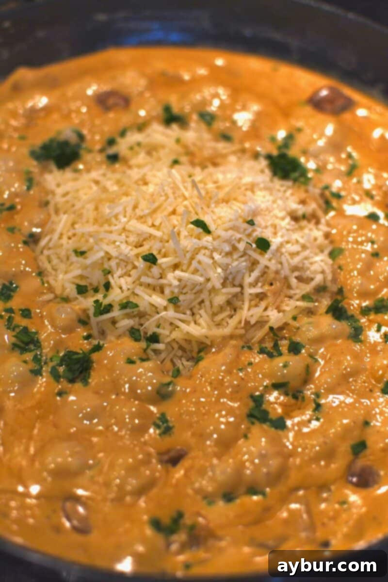 Shredded Parmesan cheese and chopped fresh parsley being added to the creamy Cajun Alfredo sauce in the pan before the pasta is mixed in.