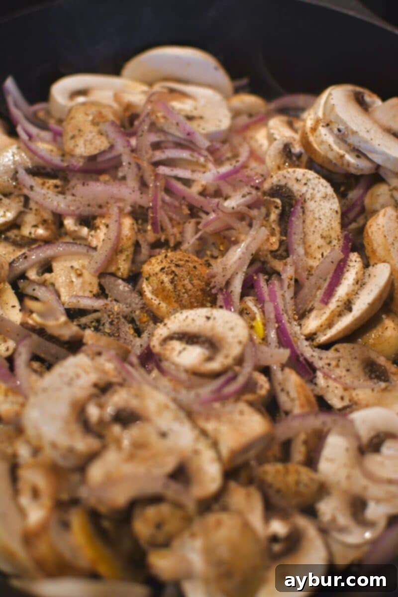 Stuffed Peppers with Philly Cheesesteak 5 Thinly sliced red onions and button mushrooms arranged in a skillet, before being cooked.