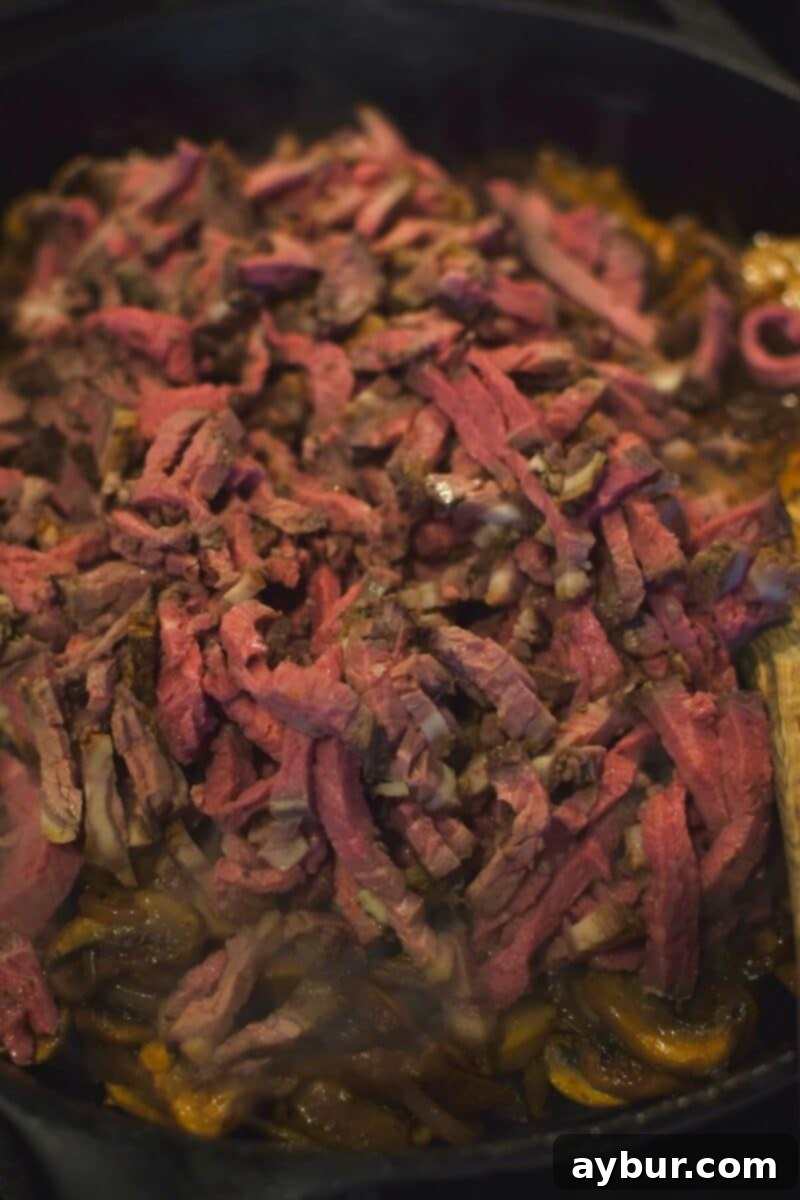 Stuffed Peppers with Philly Cheesesteak 7 Adding thinly sliced deli roast beef to the skillet with cooked onions and mushrooms, ready to be combined.