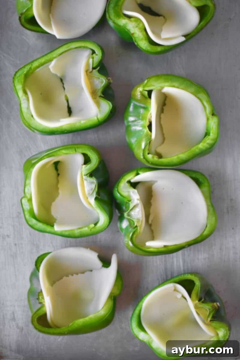 Partially roasted bell peppers, each with a single slice of provolone cheese placed inside, forming a foundational cheesy layer.