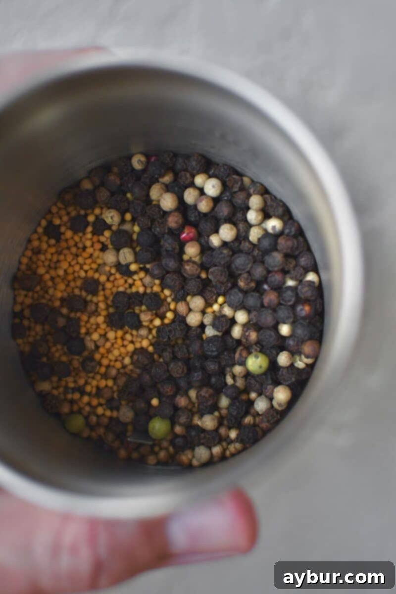 Placing whole peppercorns and various seeds into a spice grinder before beginning the grinding process.