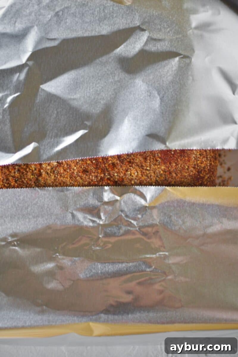 The seasoned corned beef brisket being carefully wrapped in the first layer of tin foil.