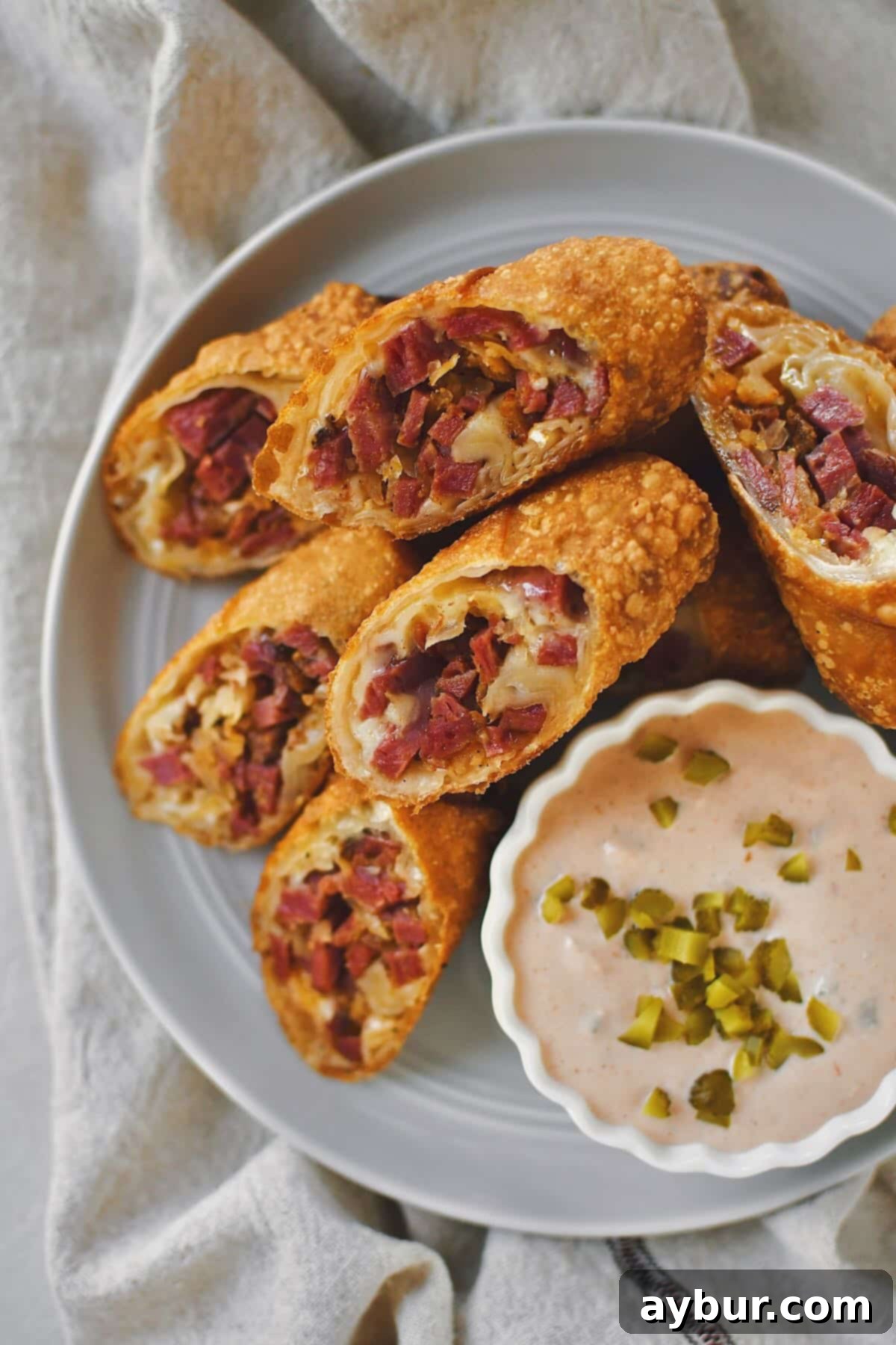 Reuben Egg Rolls sliced in half on the diagonal and served on a plate with Russian Dressing.