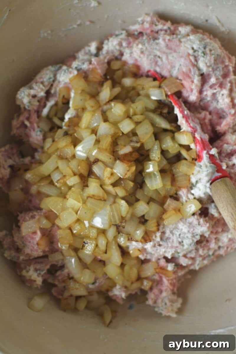 Sautéed onions, cooled, are folded into the ground turkey mixture in a bowl before forming the patties.