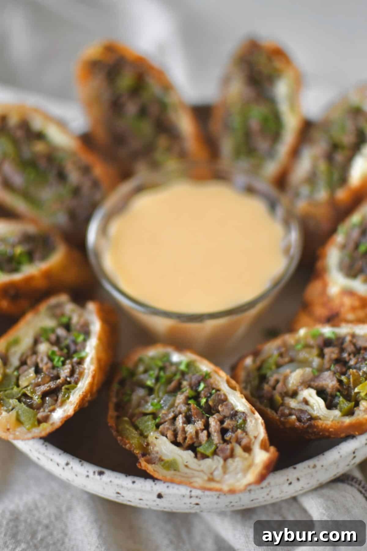 Philly Cheesesteak Egg Rolls cut in half and served with cheese sauce for dipping.