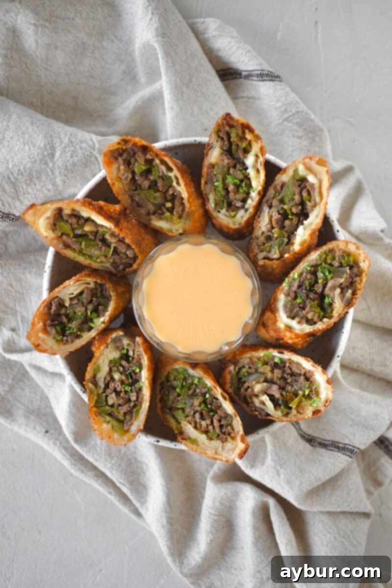 Philly Cheesesteak Egg Rolls cut in half and served with cheese sauce for dipping.