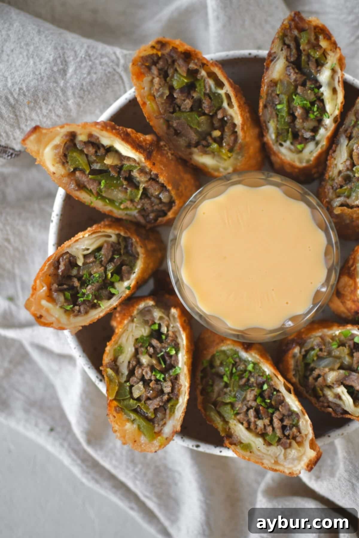 Philly Cheesesteak Egg Rolls cut in half and served with cheese sauce for dipping.
