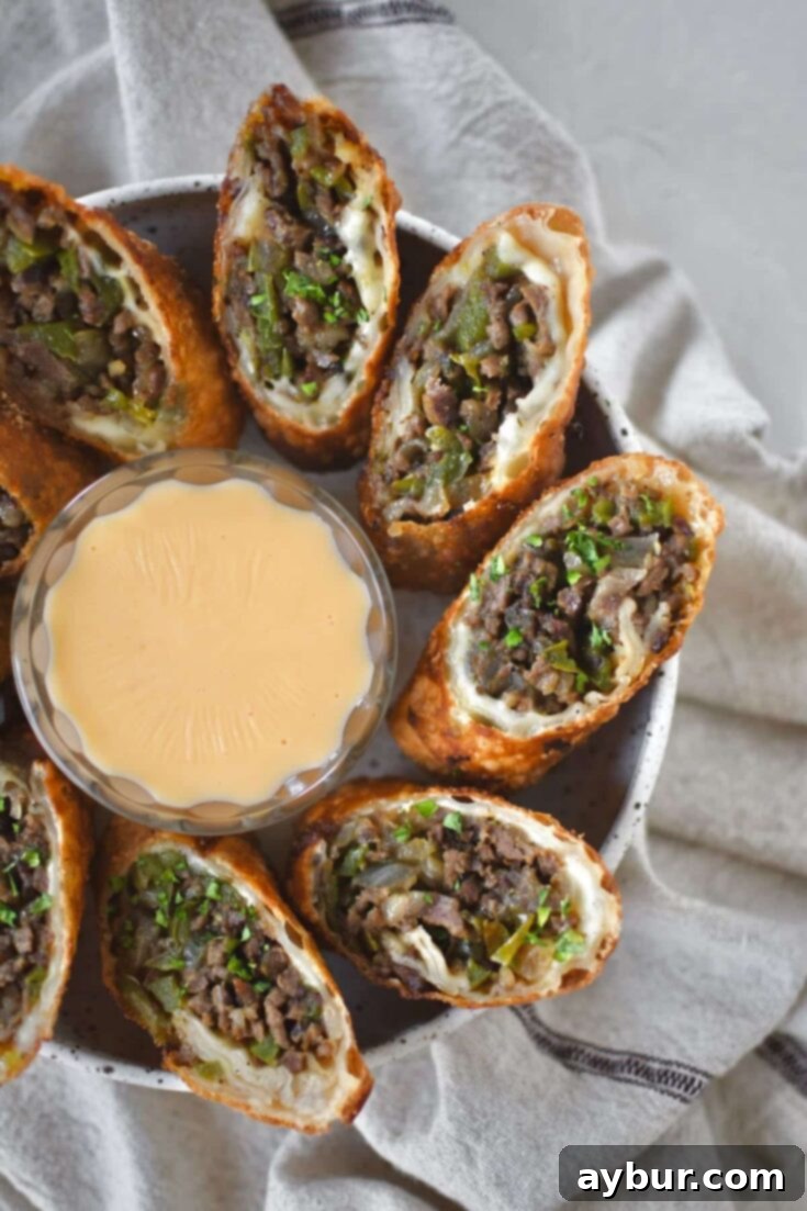 Philly Cheesesteak Egg Rolls cut in half and served with cheese sauce for dipping.