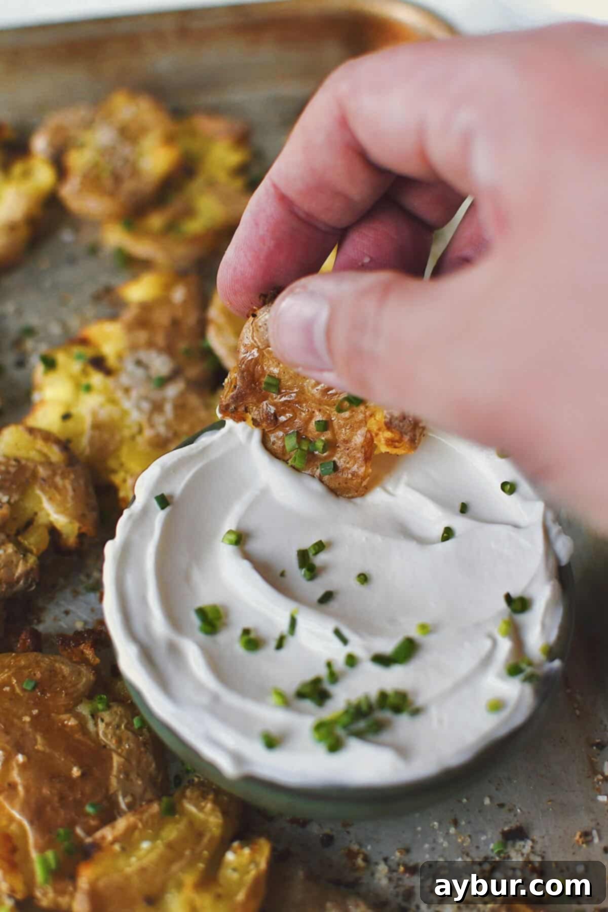 Crispy Smashed Potatoes with one being dipped in some chive sour cream.