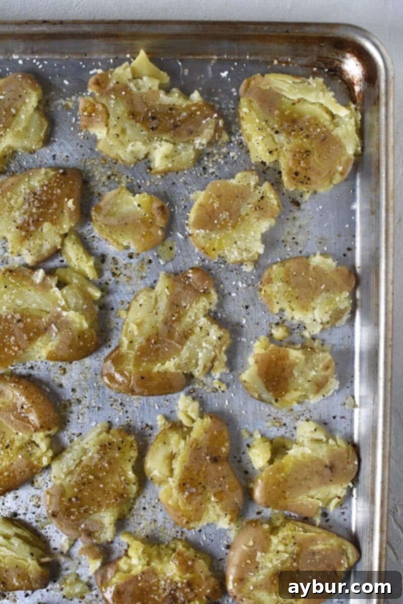 All potatoes smashed and seasoned with salt, pepper, butter, and oil on a rimmed baking sheet.