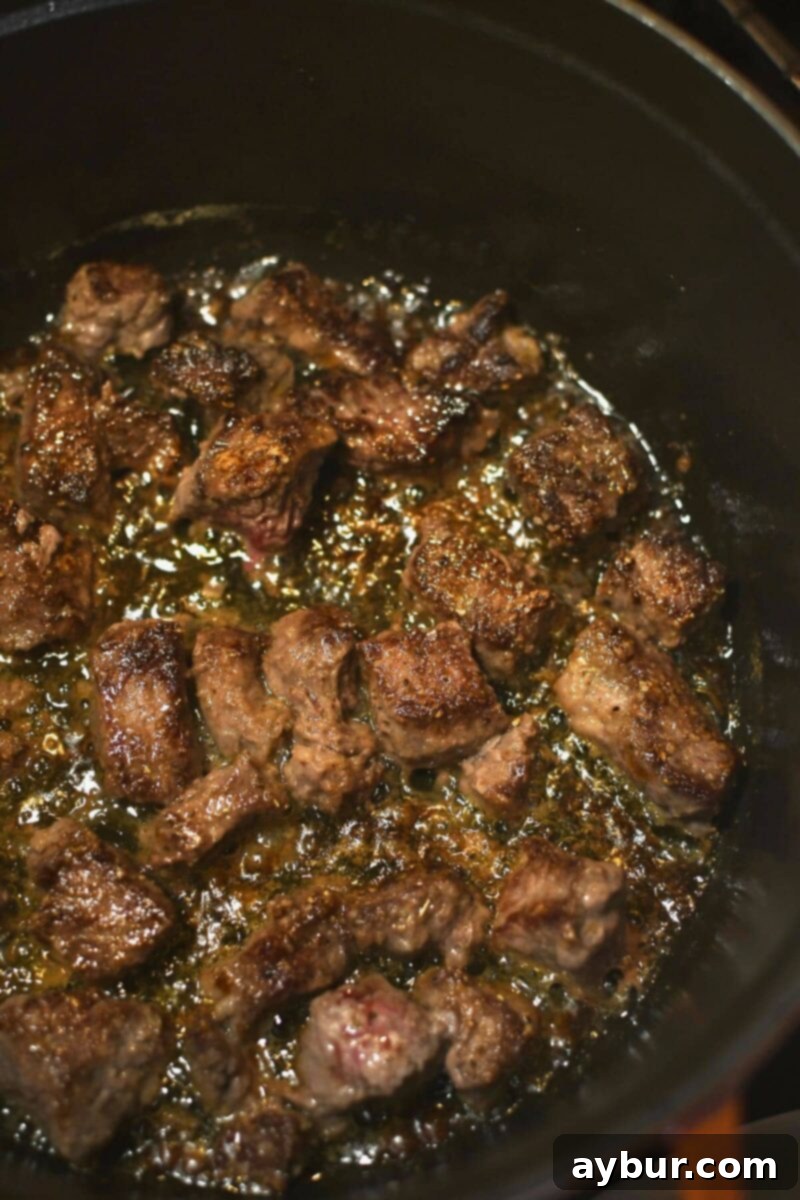 Searing the seasoned steak pieces in a large, deep pot with melted butter and olive oil until nicely browned on all sides.