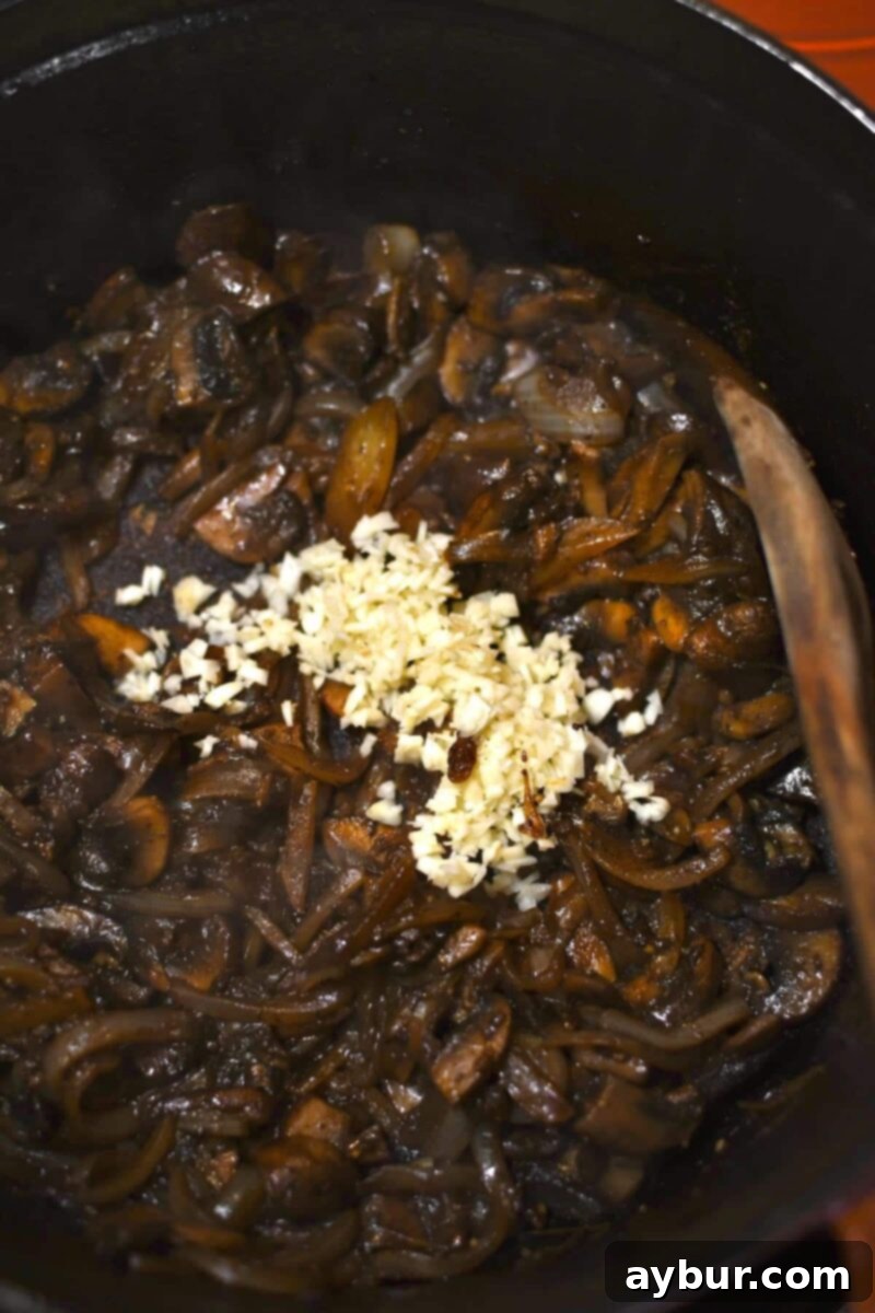 Adding minced garlic to the pot with the browned onions and mushrooms, stirring for about a minute until fragrant.