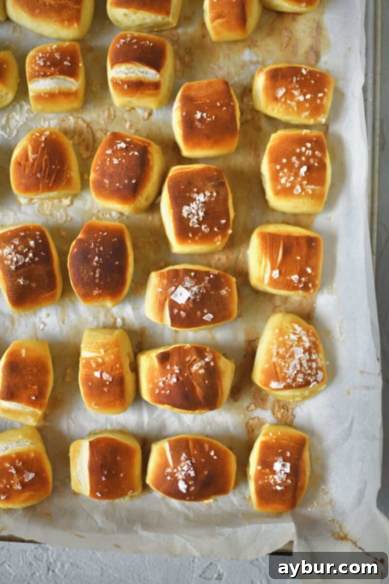 Pretzel bites lined up on a sheet pan and some of the dusted with flakey salt, after baking.