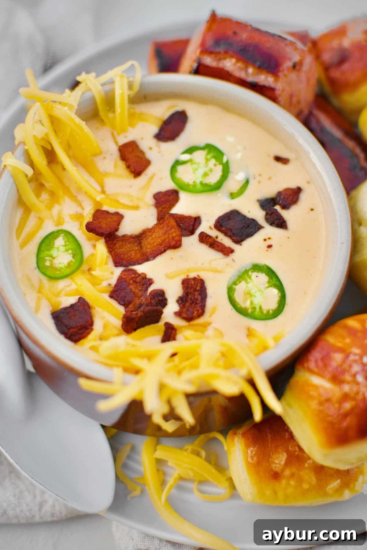 Beer Cheese Soup topped with more cheese, bacon bits, and serrano chili slices, ready to eat. Served with Kielbasa and Pretzel Bites