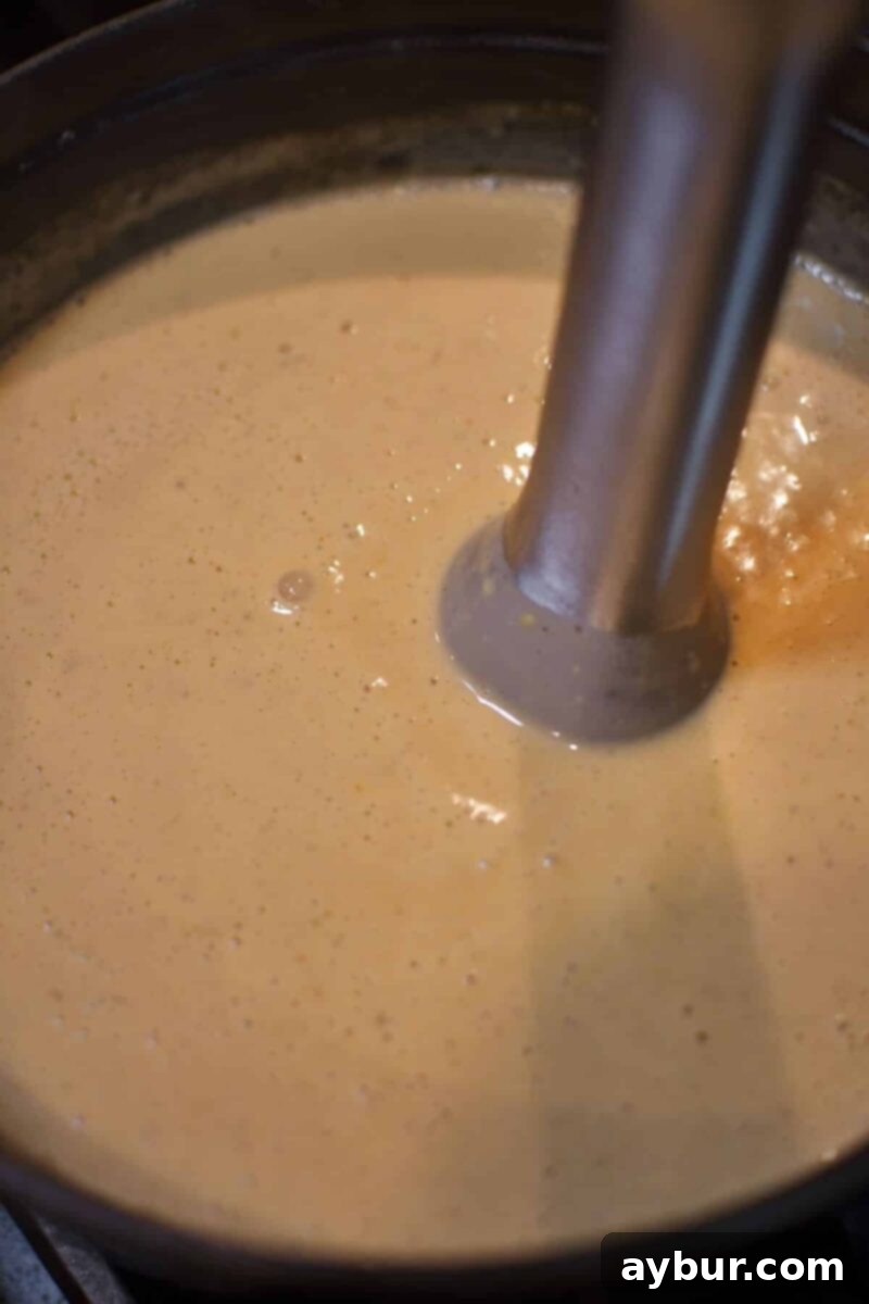 Blending the cheese into the soup using an immersion blender for a smooth finish.