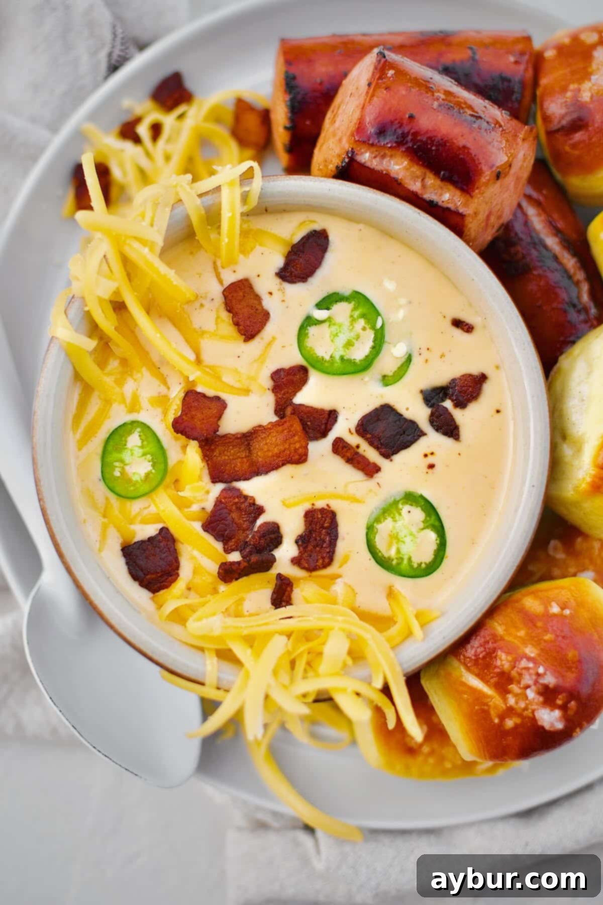 Beer Cheese Soup topped with more cheese, bacon bits, and serrano chili slices, ready to eat. Served with Kielbasa and Pretzel Bites