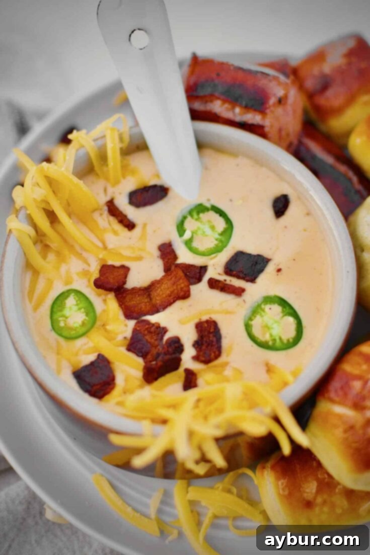 Beer Cheese Soup topped with more cheese, bacon bits, and serrano chili slices, ready to eat. Served with Kielbasa and Pretzel Bites