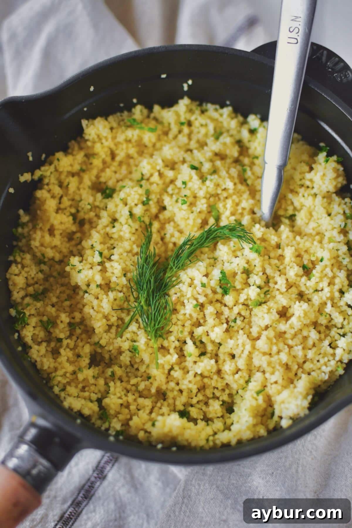 Perfectly cooked, fluffy couscous resting in a saucepan, garnished with fresh dill sprigs, ready to serve.