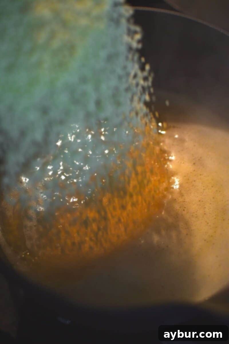 Dry couscous granules being poured into a saucepan filled with boiling chicken stock, creating a flavorful cooking base.