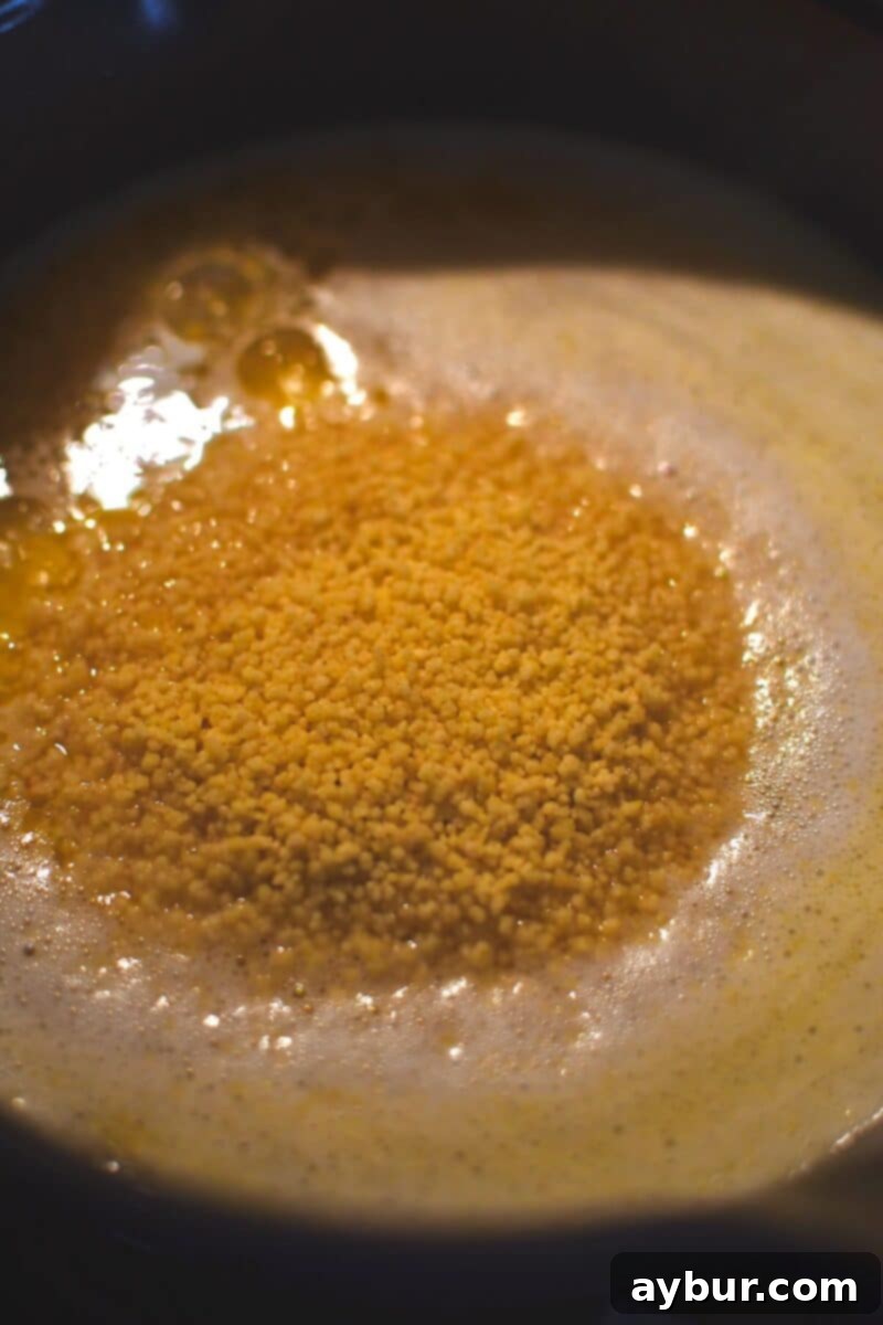 Dry couscous gently floating on the surface of hot chicken stock in a saucepan, before being stirred in and covered.