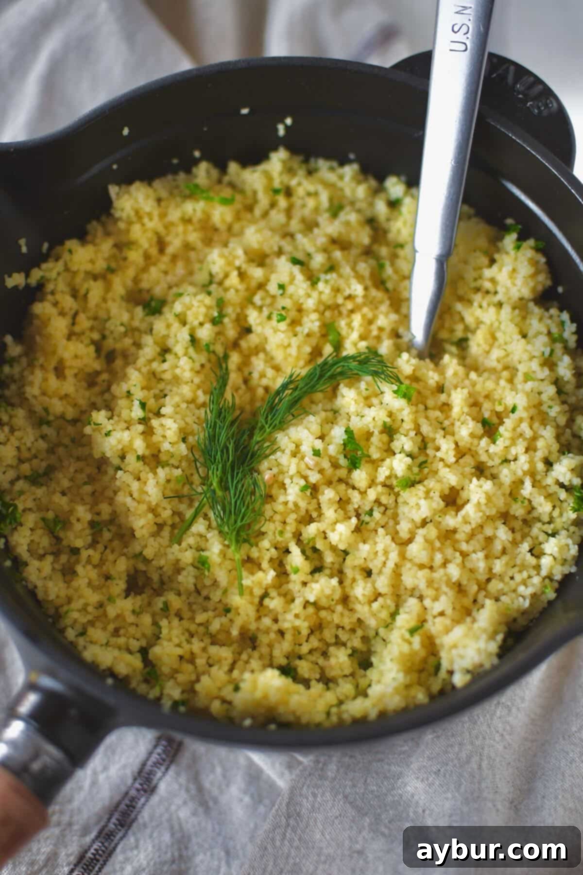 Close-up of perfectly cooked, fluffy couscous in a saucepan, beautifully garnished with fresh dill sprigs.