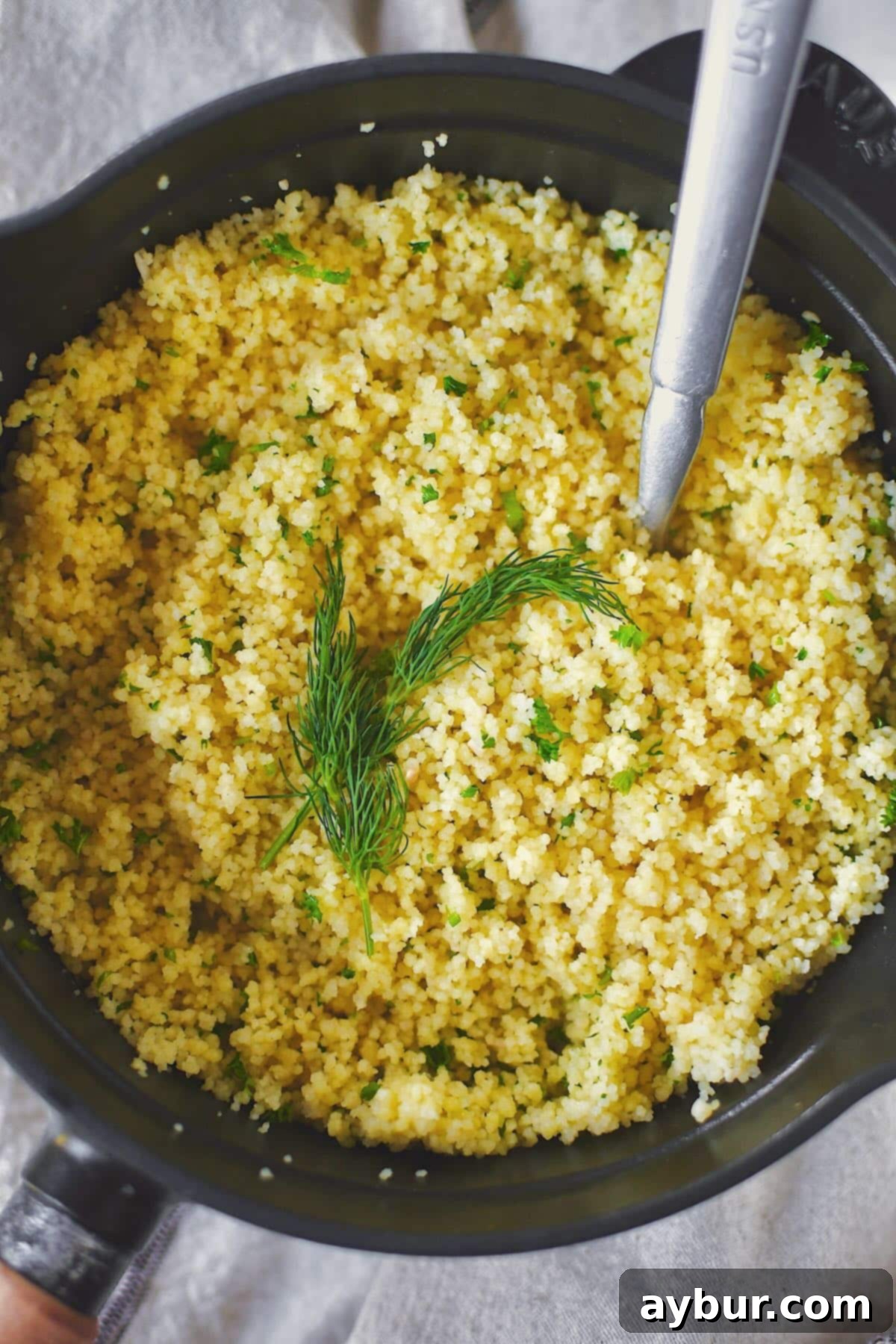 A final shot of the perfectly fluffy and flavorful couscous, garnished with fresh dill, presented in the saucepan.