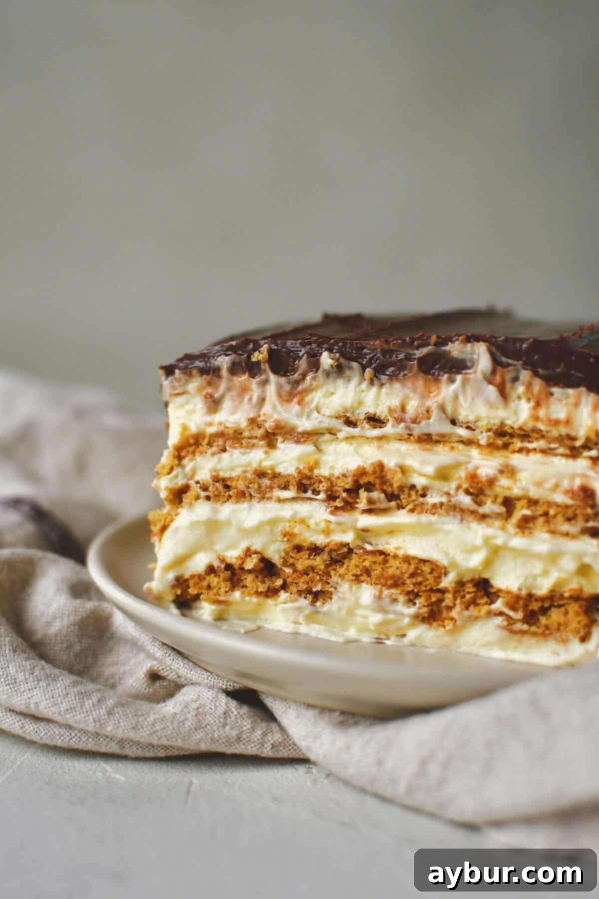 A perfectly portioned slice of Eclair Cake, glistening with chocolate frosting and creamy filling, presented on a white plate, ready to be savored.