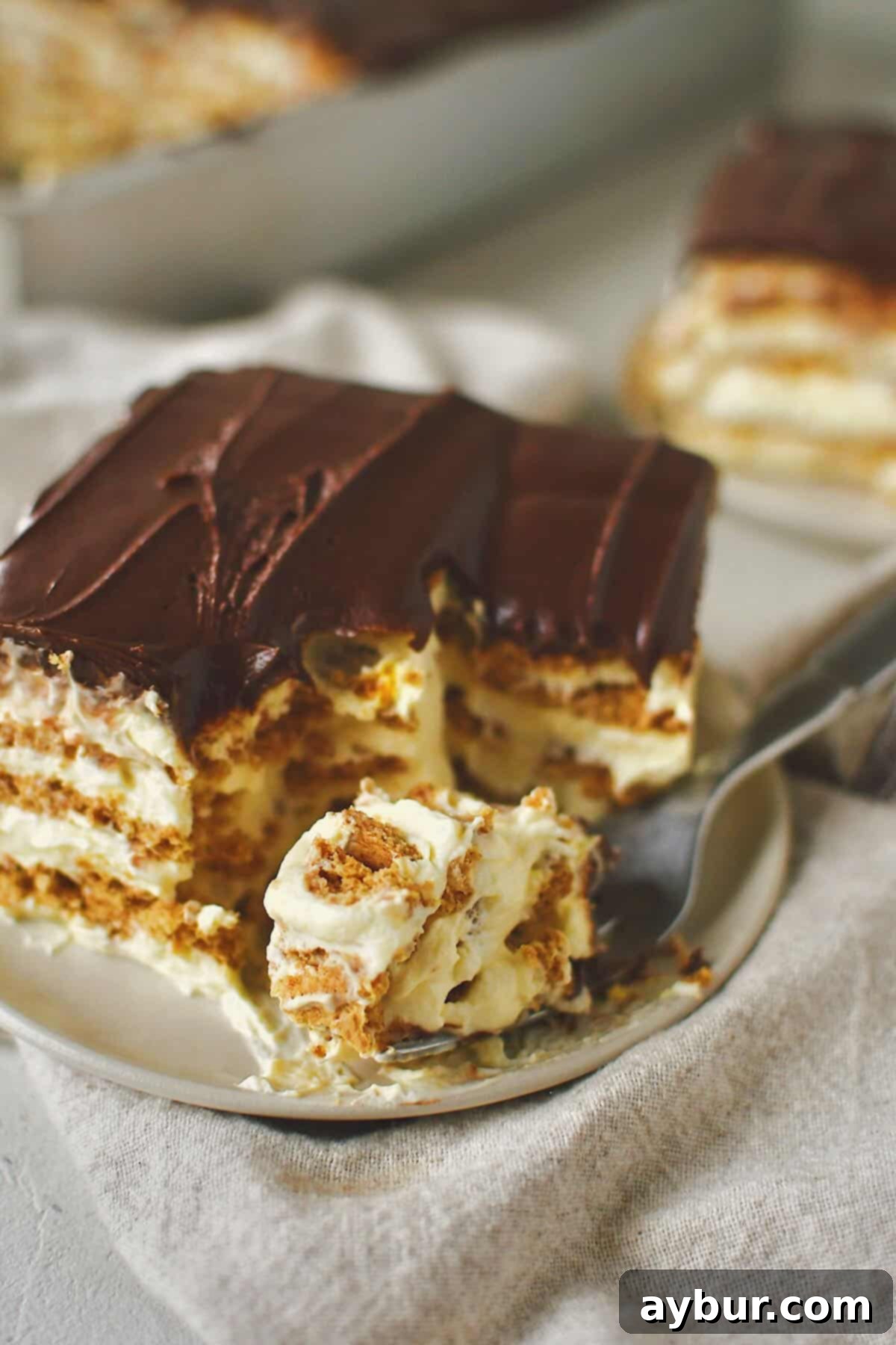 A fork taking a delicious bite out of a slice of Eclair Cake, showcasing the creamy filling and softened graham crackers.