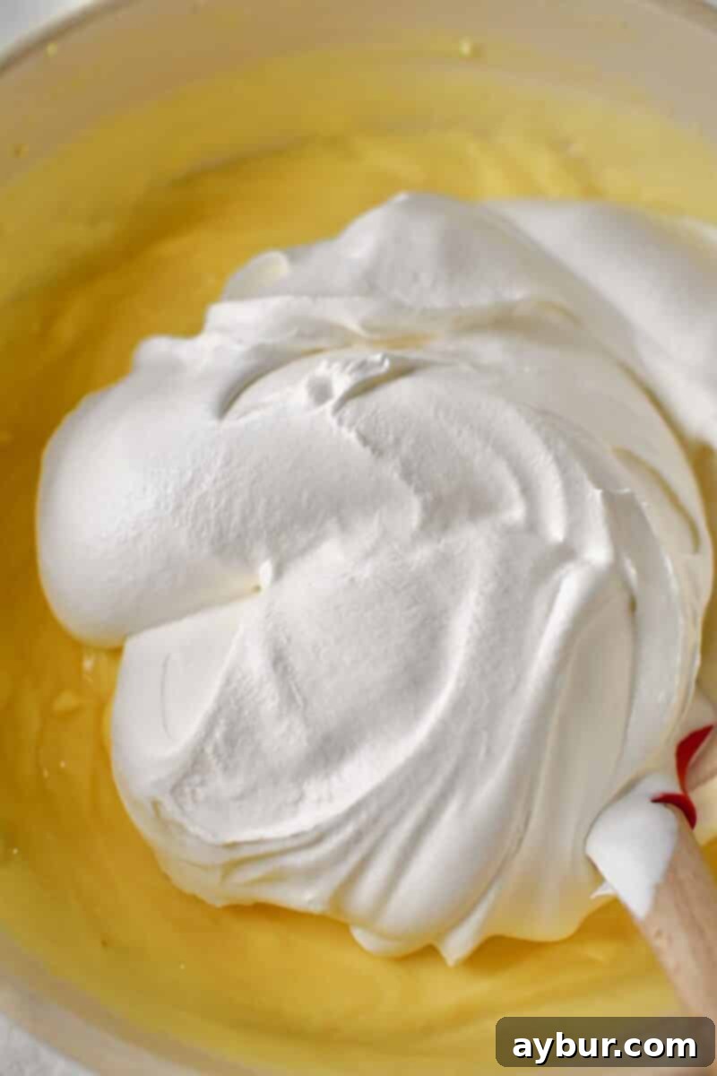 A close-up shot of fluffy whipped topping being gently folded into the prepared pudding mixture, creating a light and airy custard.