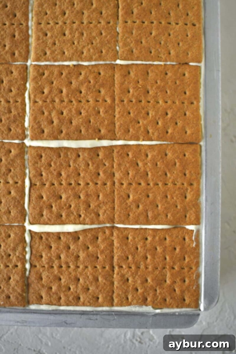 Adding additional layers of graham crackers and pudding mixture, showing the build-up to 5 distinct cracker layers.