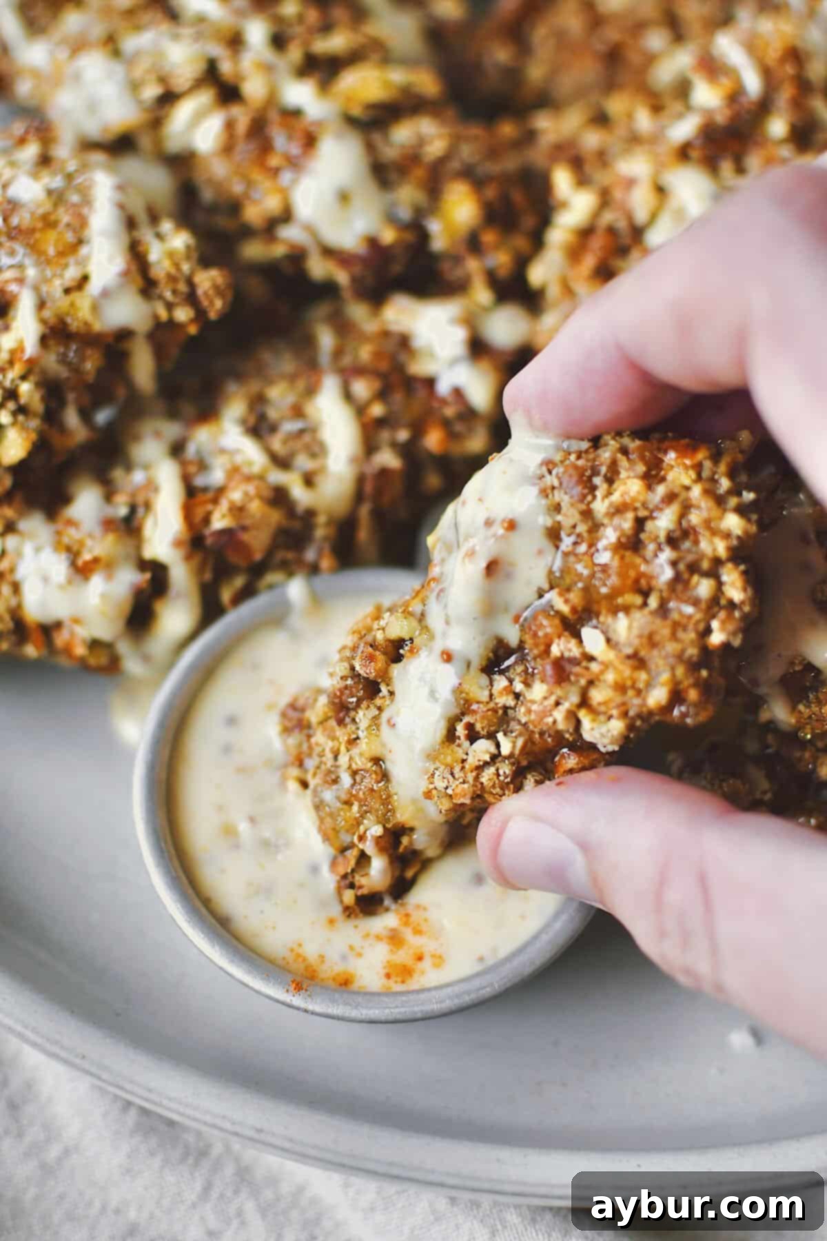 Crispy Pecan Chicken 2 A golden-brown piece of Pecan Crusted Chicken being dipped into a creamy honey mustard sauce, highlighting its crispy texture and readiness to eat.