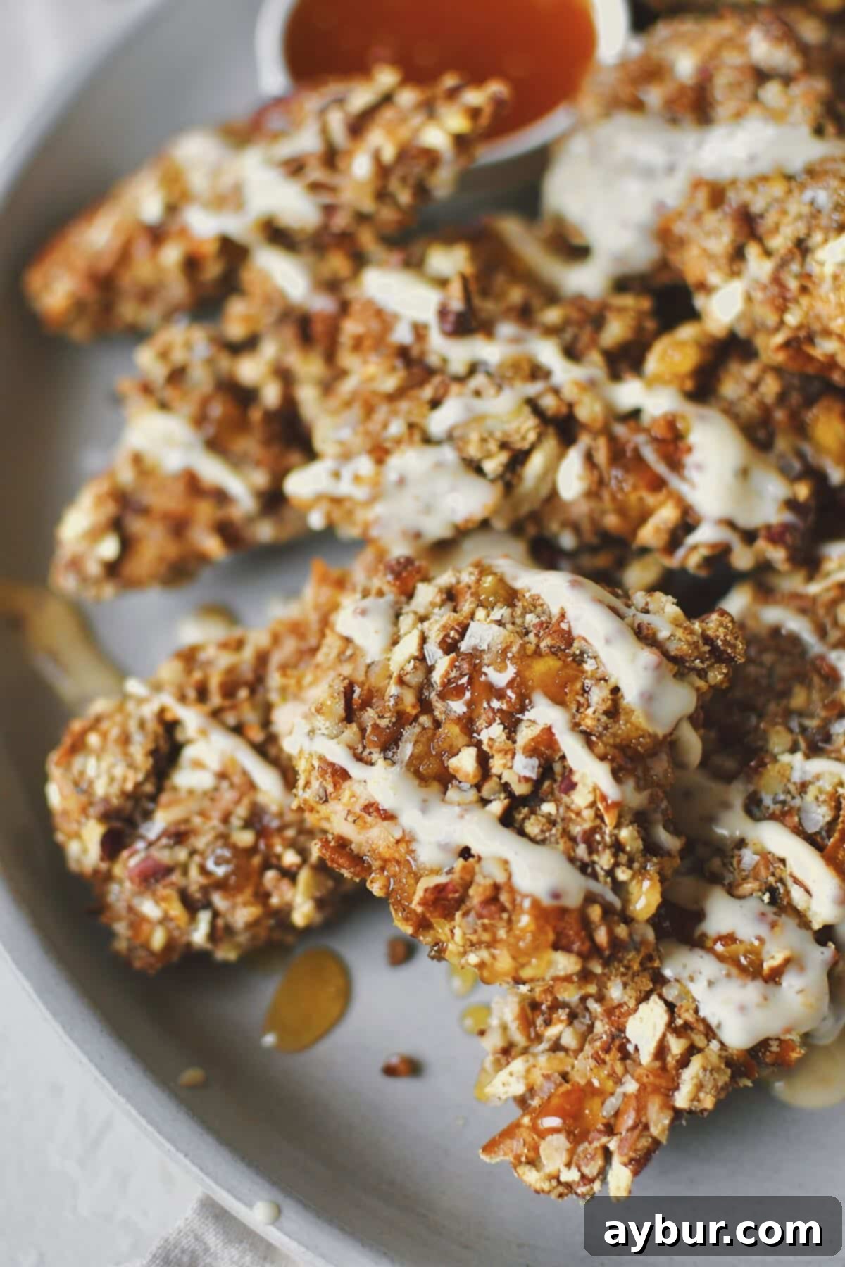 Crispy Pecan Chicken 8 A wide shot of a platter of Pecan Crusted Chicken, garnished with fresh parsley and drizzled with honey, alongside a serving of honey mustard dipping sauce. The golden-brown crust is clearly visible.