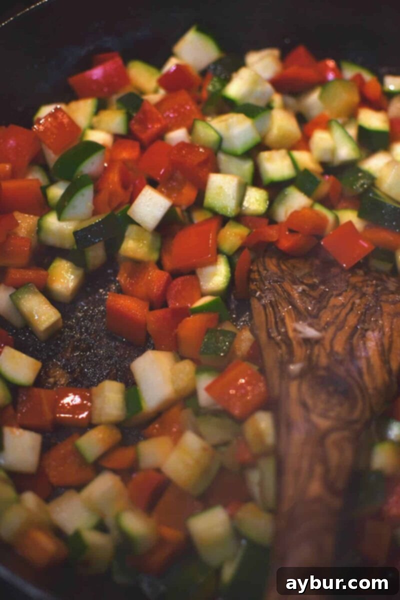 Adding the veggies to the same pan after the chicken has been cooked.