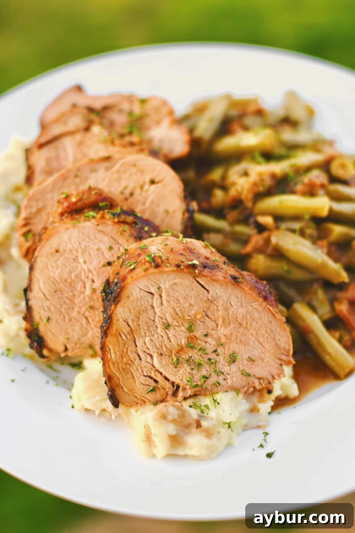 Slices of grilled pork tenderloin served on a plate with creamy mashed potatoes underneath and southern green beans on the side.