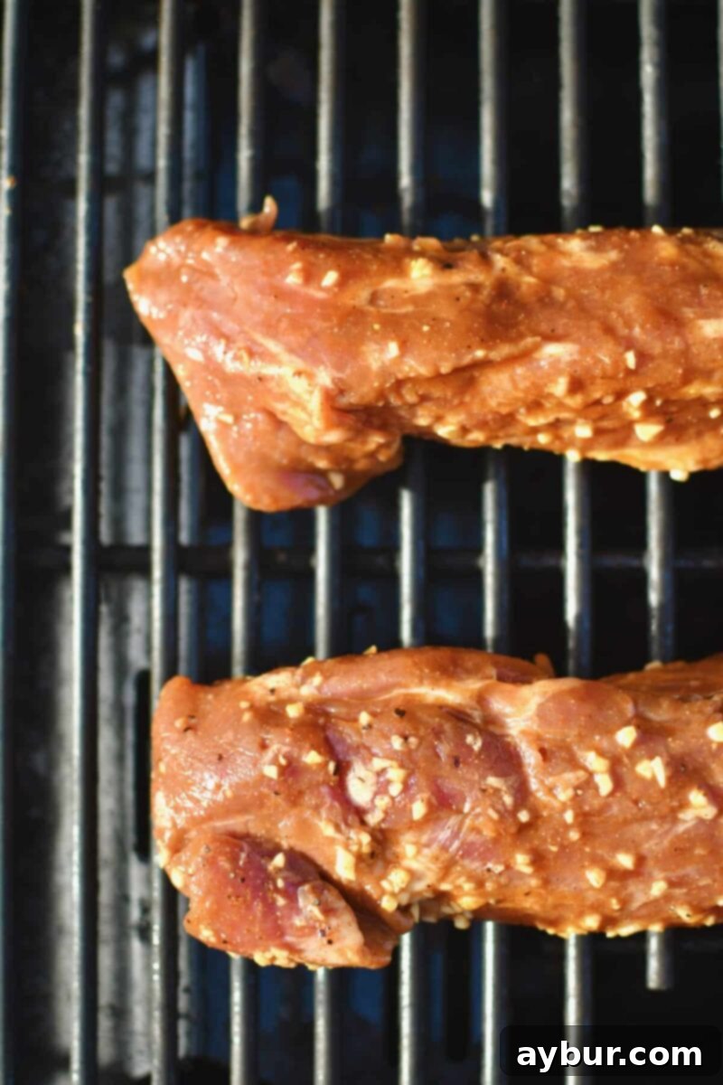 Marinated pork tenderloins just out of the marinade and placed on a hot grill, beginning to sear.