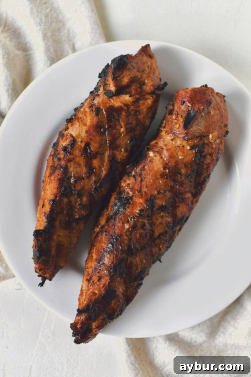 Two grilled pork tenderloins resting on a plate immediately after being removed from the grill.