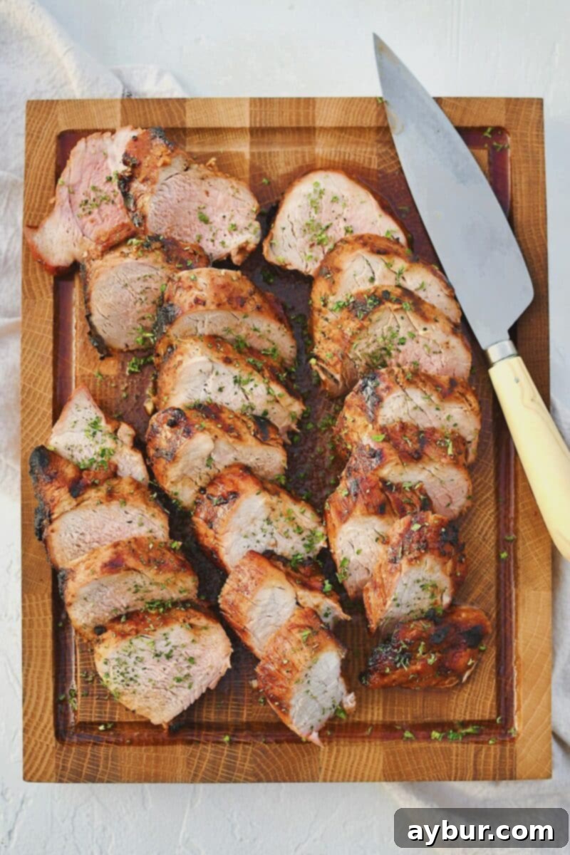 Grilled Pork Tenderloin beautifully sliced and arranged on a cutting board, with a chef's knife nearby.