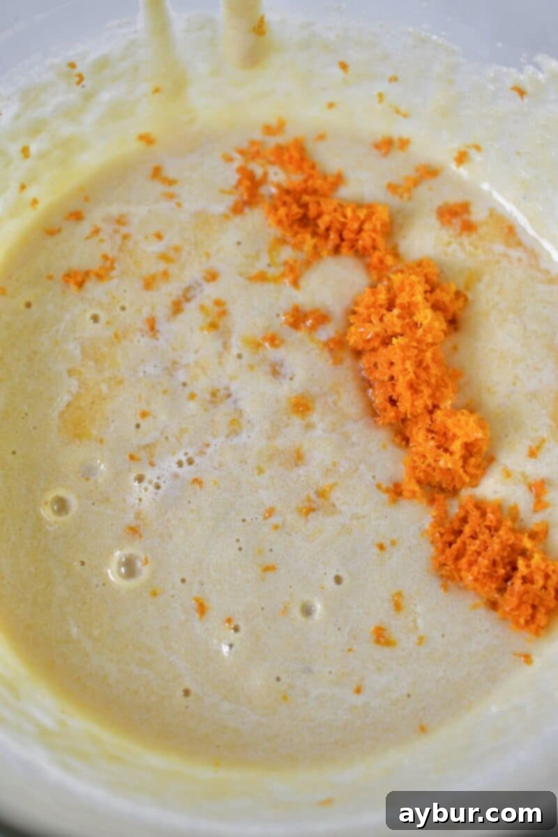 Incorporating fresh tangerine juice and zest into the fluffy cake batter inside the mixer bowl, ensuring a burst of citrus flavor.