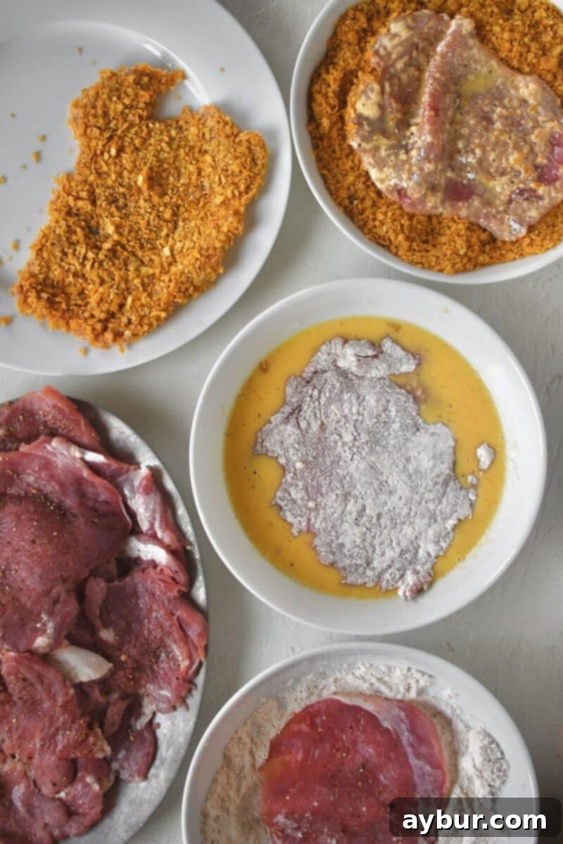 Pan-Fried Pork Perfection 5 A breading station set up with seasoned flour, egg wash, and crushed cornflakes, ready for coating pork cutlets.