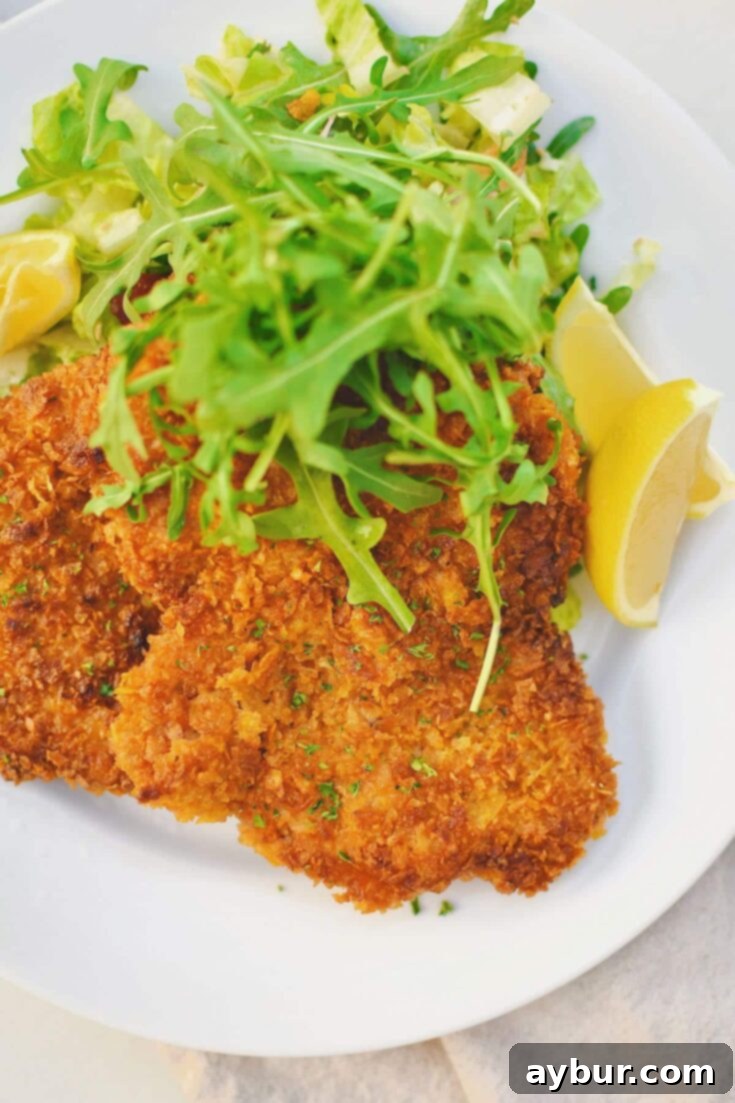 Pan-Fried Pork Perfection 10 Pork Schnitzel on a plate, served with an arugula salad and lemon wedges.