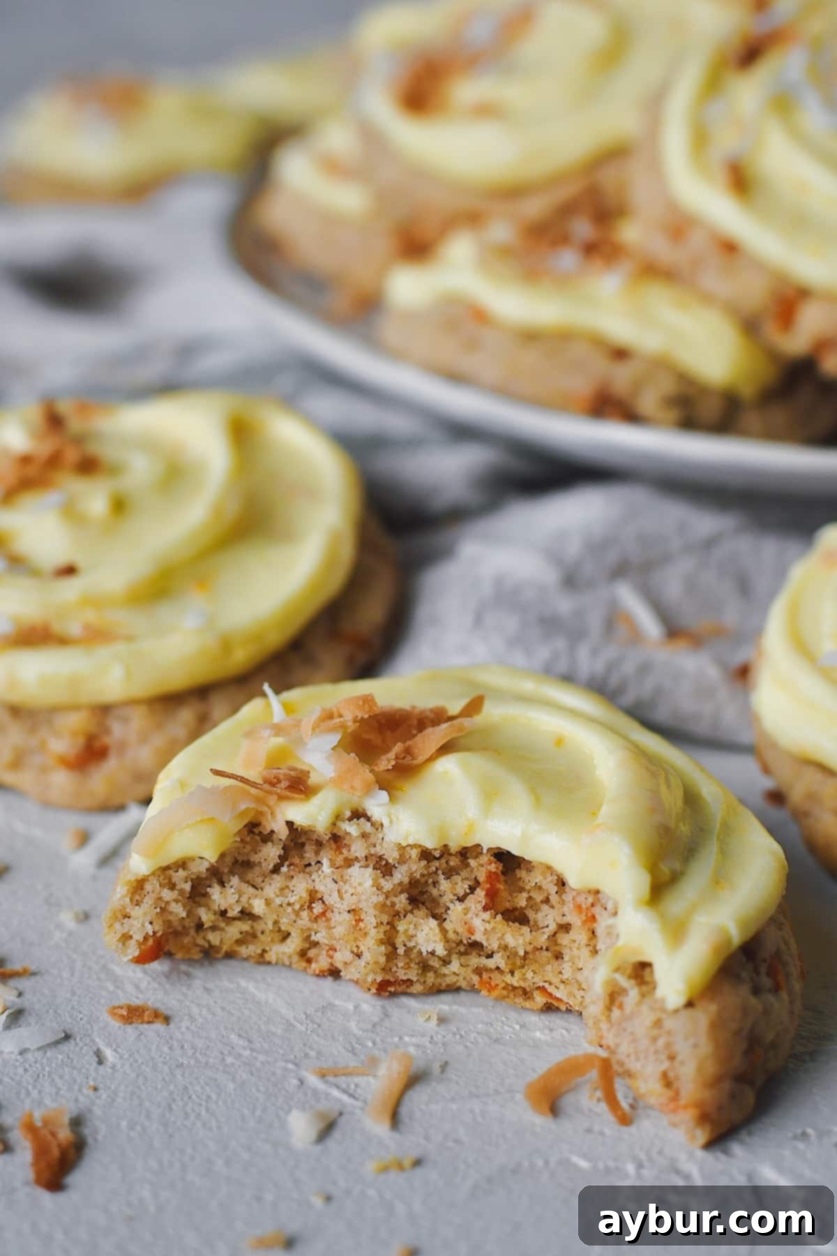 Spiced Carrot Cake Cookies 2 Carrot Cake Cookies topped with toasted coconut and laid out on a table, with a bite taken out of one. These homemade treats offer a taste of spring with their fluffy texture and tangy orange frosting.