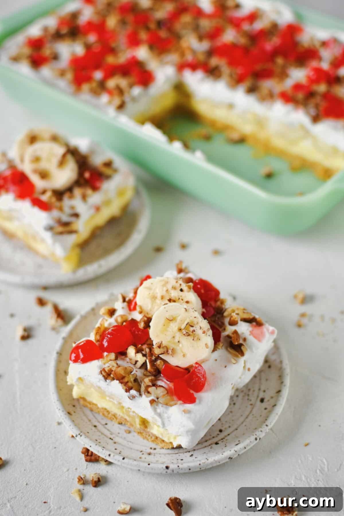 Ultimate Banana Split Cake 2 A delectable Banana Split Cake in a glass baking dish, with a couple of slices already removed, revealing the creamy layers. Fresh banana slices and a sprinkle of chopped pecans garnish the individual servings, ready to be enjoyed.